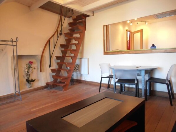 A modern interior with a wooden spiral staircase, a dining area with two chairs, a table, and a large mirror reflecting a door.