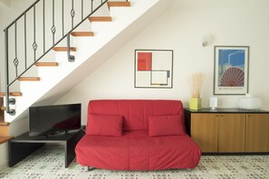 Un soggiorno moderno con un divano rosso, una televisione a schermo piatto, una scala con gradini in legno, un quadro astratto incorniciato e un poster con l'immagine di una nave.