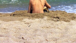 A child sitting on a sandy beach facing the ocean.