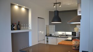 Una cocina moderna con encimera oscura, una lámpara colgante y un microondas.