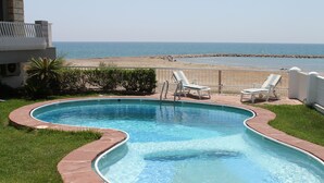 A swimming pool with a curved edge, surrounded by a brick border, and two lounge chairs facing the ocean. - Luxury beachside villa  with private pool, terrace and sea views. (Benicassim)