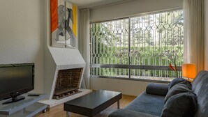 A modern living room with a fireplace, a sofa, a TV, and a large window with a view of greenery. - Luxury beachside villa  with private pool, terrace and sea views. (Benicassim)