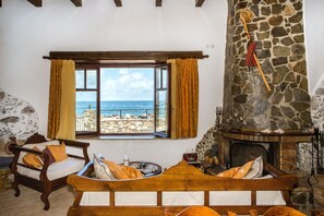 Una habitación acogedora con chimenea de piedra, una cama de madera y vista al mar por una ventana.