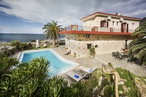 Un edificio de dos pisos con piscina, mobiliario exterior y vista al mar.