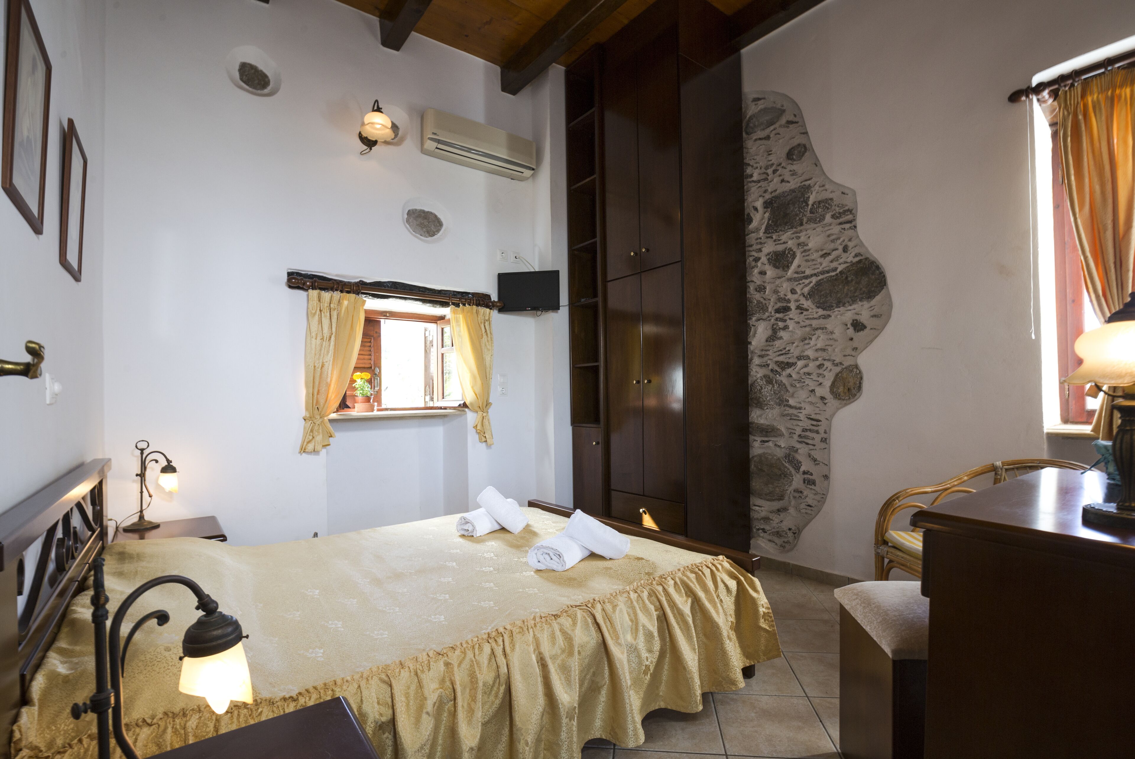Ein Schlafzimmer mit Bett, Schreibtisch, Stuhl, einem Fenster mit Vorhängen und einer Steinwand.