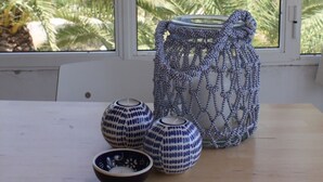 Een tafel met drie keramieken schalen en een rieten mandje bij een raam met uitzicht op palmbomen.