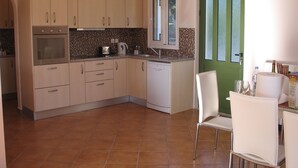 Una cocina con armarios de colores claros, horno empotrado, lavavajillas y una puerta verde.