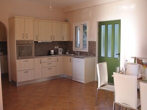 Una cocina con armarios de colores claros, horno empotrado, lavavajillas y una puerta verde.