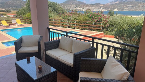Un balcón con mobiliario de mimbre, una piscina y vistas al mar y a las montañas.