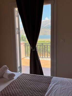Habitació d'hotel amb un llit, una finestra amb cortines i vista a un balcó i un paisatge.