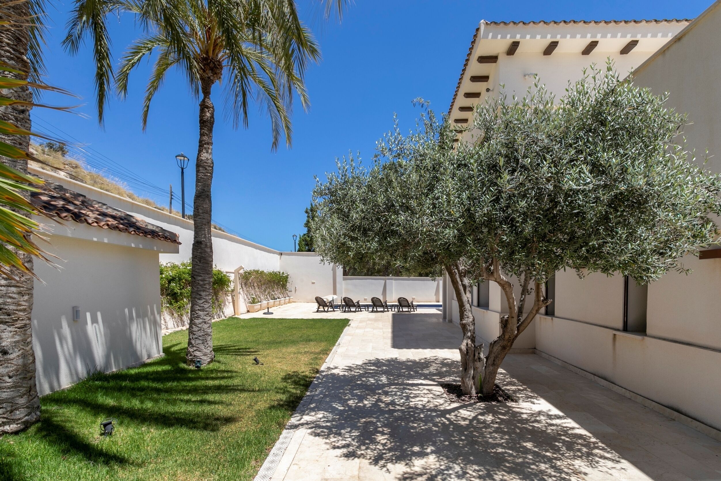 Un cortile con un’area salotto, palme e un edificio con tetto in tegole.