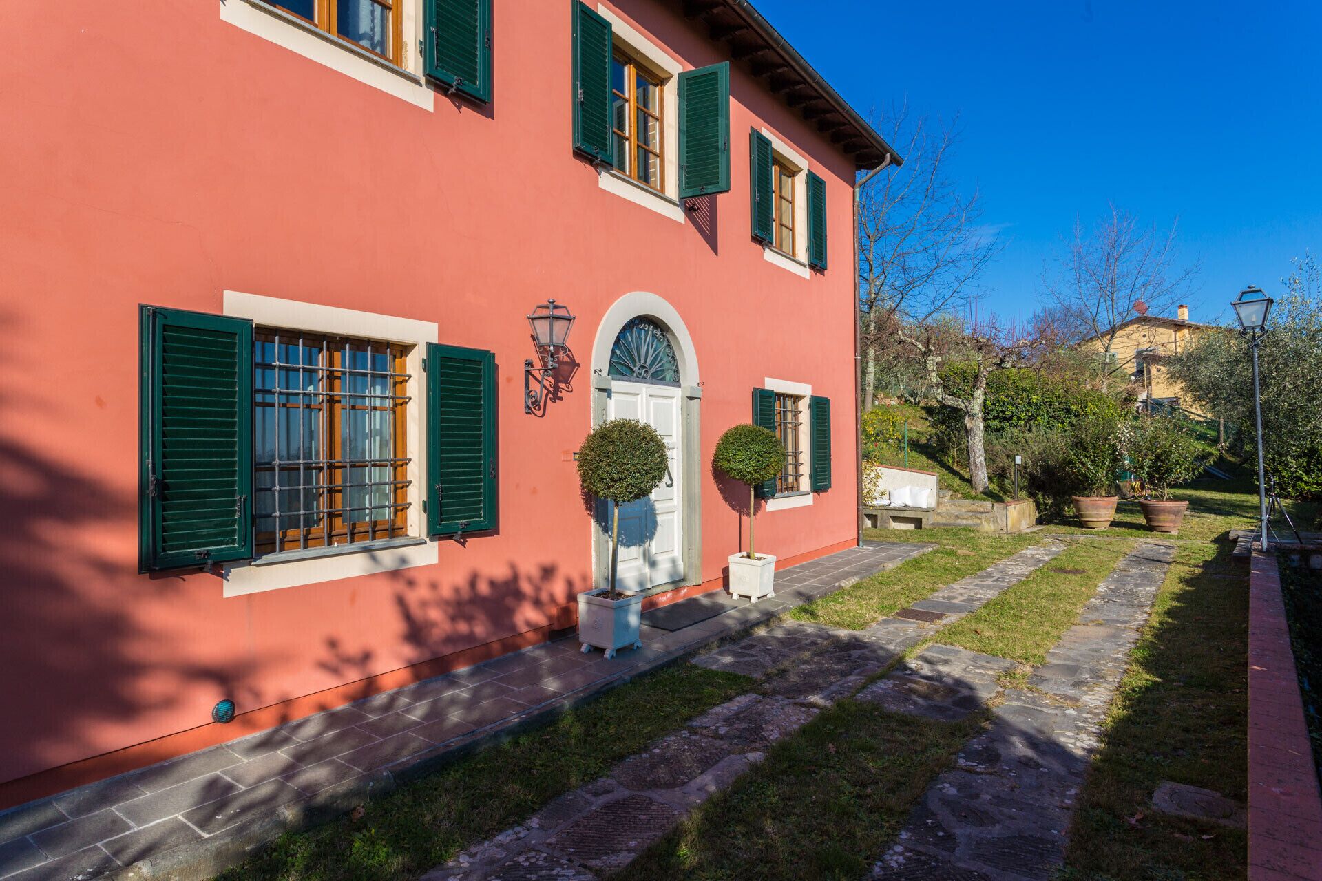 Un edificio rosso con persiane verdi, una porta bianca e un piccolo giardino con un vialetto.