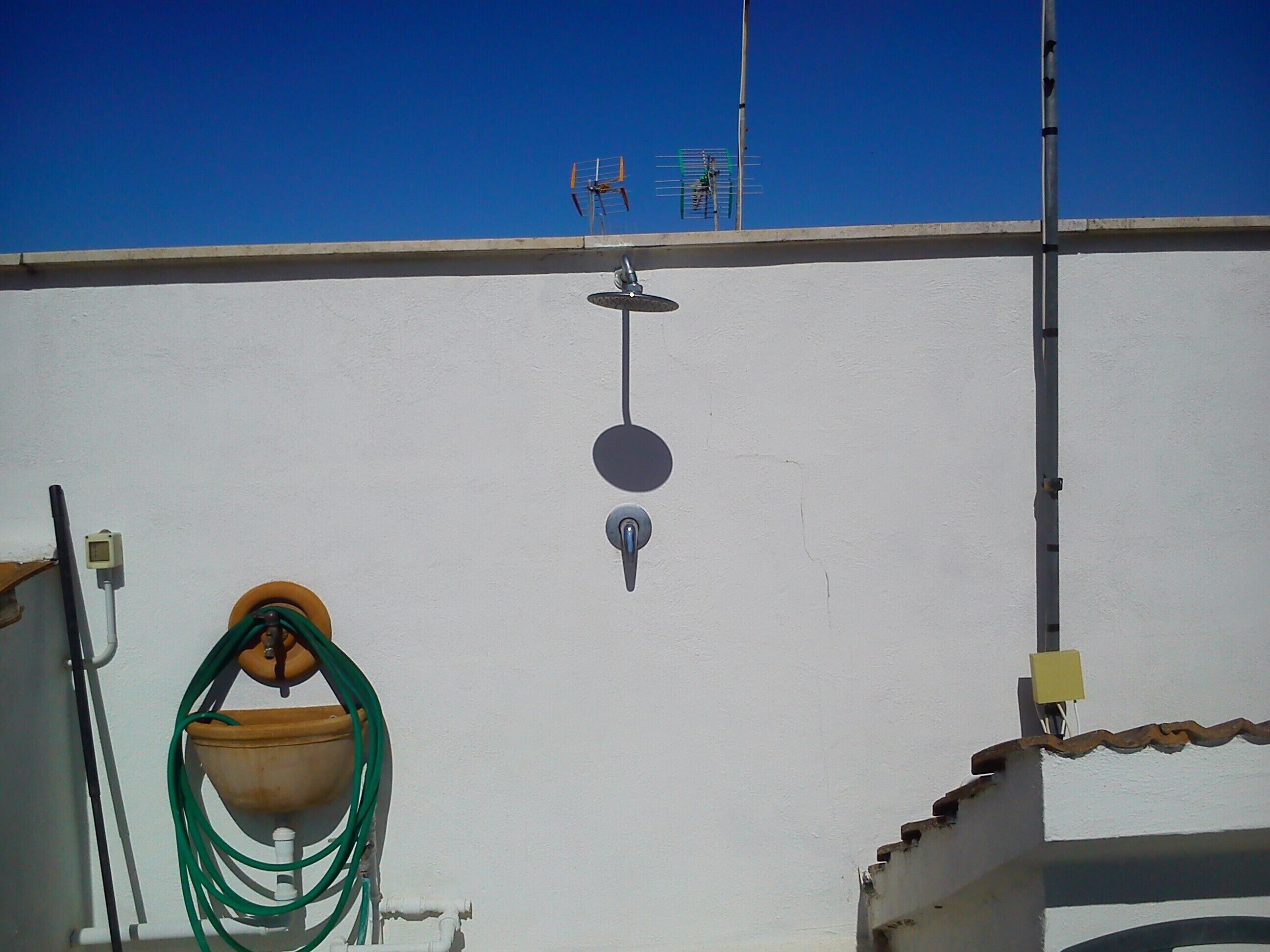 Un edificio blanco con una antena parabólica, un tanque de agua y una manguera.