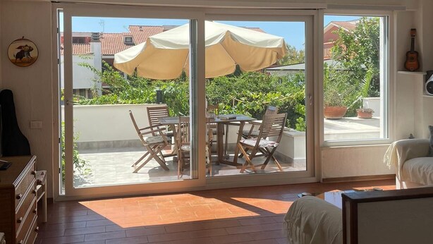 Een ruime kamer met een grote schuifglazen deur naar een terras. De kamer heeft een bed, een gitaar en een klein tafeltje.