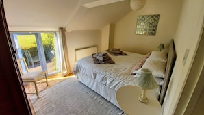A bedroom with a large bed, a small table, and a view of the outdoors through a sliding door. - Rural Holiday Cottage with Wonderful Countryside Views on Friendly Smallholding. (Stockland)
