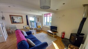 A living room with a blue sofa, a television, a fireplace, and a dining area with a table and chairs. - Rural Holiday Cottage with Wonderful Countryside Views on Friendly Smallholding. (Stockland)