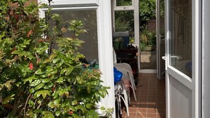 Une véranda avec un mur en briques, un sol carrelé et une petite table entourée de chaises.