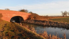 Un pont en briques enjambant une rivière paisible, bordée de rives verdoyantes et de roseaux.