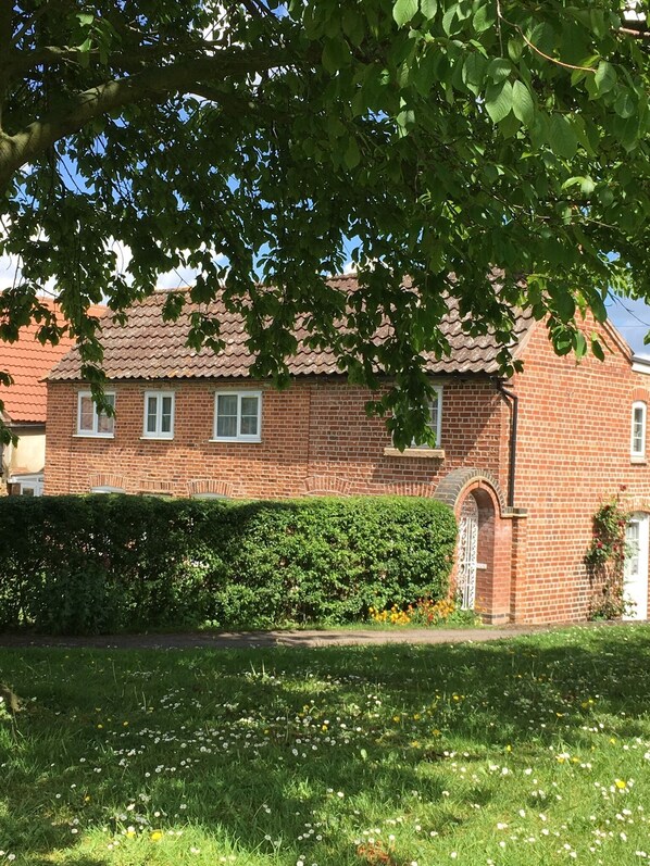 Une maison en briques avec un toit en tuiles, un petit jardin fleuri et une haie devant.