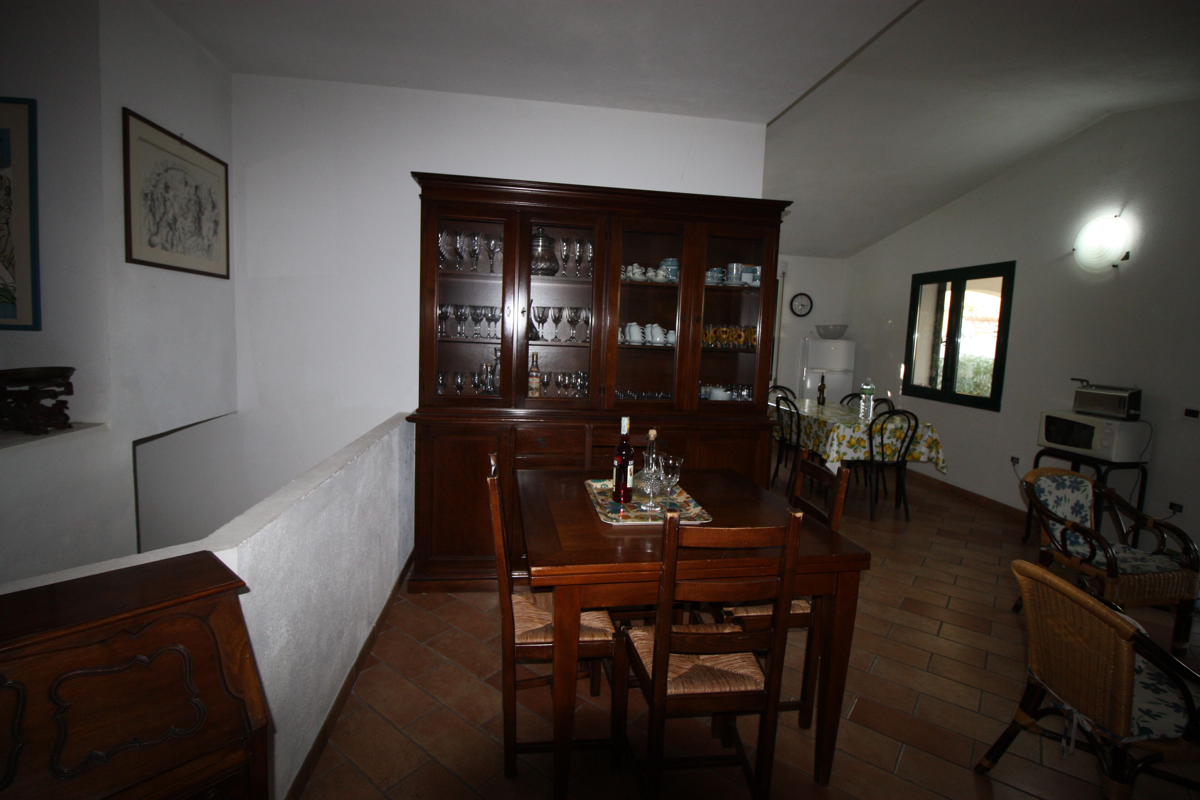 A dining area with a wooden table, chairs, a cabinet with glassware, and a clock on the wall.