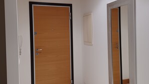 Un pasillo con una puerta de madera, una lámpara en la pared y un espejo.