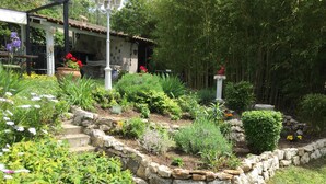 A garden with a stone retaining wall, various plants, and a small structure with a tiled roof.