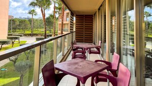 A balcony with tables and chairs, overlooking a landscaped garden with palm trees and a building in the background. - Herdade dos Salgados, T2 12B_2C, Vila das Lagoas (Albufeira)