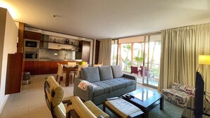 A compact living space with a kitchenette, a sofa, a dining table, and a balcony with curtains. - Herdade dos Salgados, T2 12B_2C, Vila das Lagoas (Albufeira)