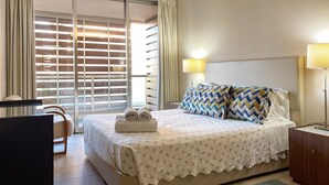 A hotel room with a bed, a desk, a chair, a lamp, and a view through the window. - Herdade dos Salgados, T2 12B_2C, Vila das Lagoas (Albufeira)