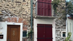 A stone building with two wooden doors, one with a brass knocker and the other with a metal handle. There are potted plants on the ground and a small window on the wall.