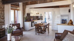 A spacious living area with a dining table and chairs, a brown leather sofa, and a kitchen in the background.