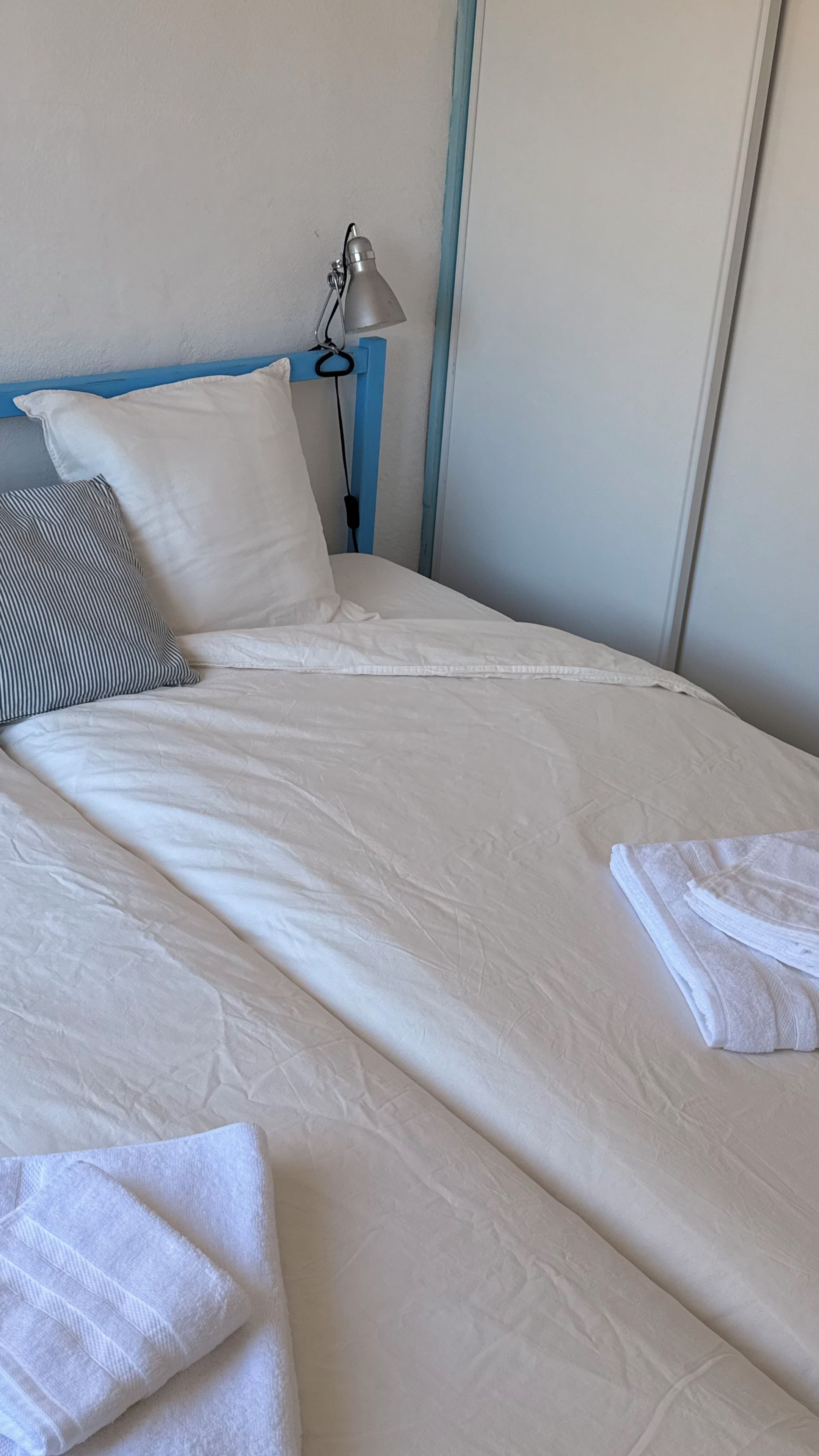Cama bem arrumada com edredom branco, toalha branca dobrada e travesseiro listrado.