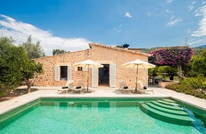 A stone villa with a swimming pool, outdoor seating, and a garden.