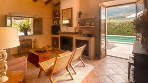 Una sala de estar acogedora con chimenea, un sofá, una silla de mimbre y vistas a una piscina a través de un ventanal.