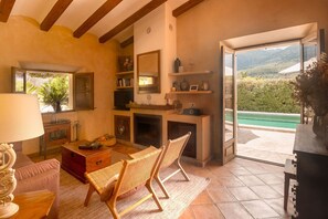 A cozy living room with a fireplace, a sofa, a wicker chair, and a view of a pool through an open door.