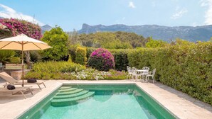 Una piscina con vistas a montañas, rodeada de exuberante vegetación y mobiliario exterior blanco.