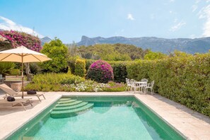 A swimming pool with a view of mountains, surrounded by lush greenery and white outdoor furniture.