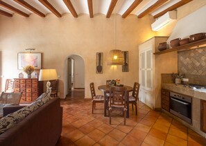 A cozy living room with a sofa, a dining table with chairs, a kitchen area with a stove, and a hallway.