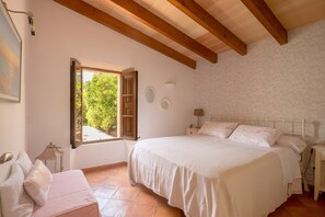 A bedroom with a large bed, a window with open shutters, a bedside table, and a nightstand.