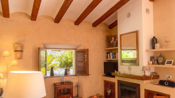 Una sala de estar acogedora con chimenea, vigas de madera, televisor y ventana con vista a follaje.