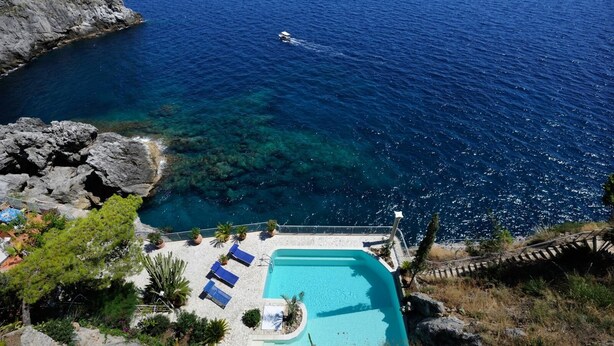 Un complejo turístico frente al mar con piscina, sillas de descanso y costa rocosa.