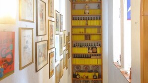 Un pasillo estrecho con obras de arte enmarcadas en las paredes, una exhibición amarilla de botellas y un radiador blanco.