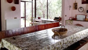 Comedor con una mesa larga cubierta con un mantel floral, bancos de madera y una lámpara colgante.