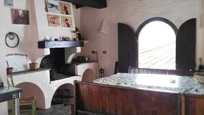 Cocina rústica con suelo de piedra, vigas de madera, un banco de madera, una mesa y una lámpara colgante.