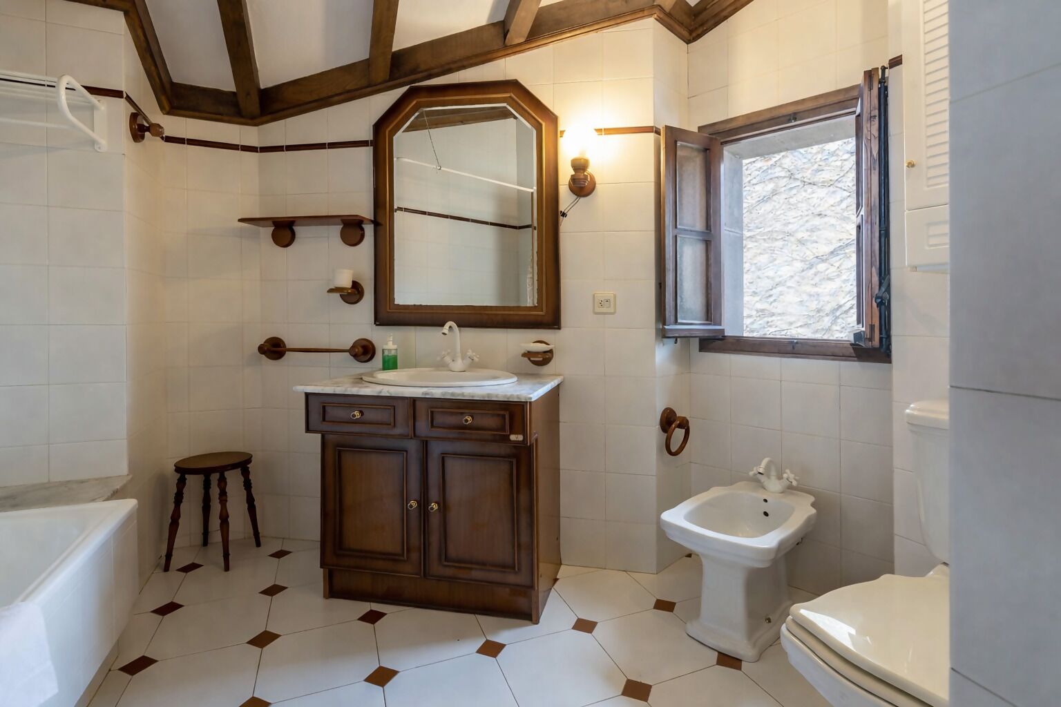 Ein Badezimmer mit einem Holzausziehtisch, einem Standwaschbecken, einem Spiegel, einem Fenster und einer Toilette.