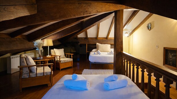 Een gezellige kamer met een houten plafond, een bed met witte lakens, een stoel en een tafel met een lamp.