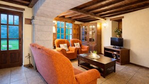 Een ruime woonkamer met een hoge plafond, houten balken, een open haard en een televisie.