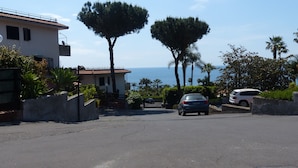 A residential street with a house, two tall trees, and a view of the sea. - Spacious and bright apartment with terrace and beautiful sea views (Aci Castello)