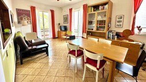 A dining area with a wooden table and chairs, a television, and a bookshelf. - Spacious and bright apartment with terrace and beautiful sea views (Aci Castello)