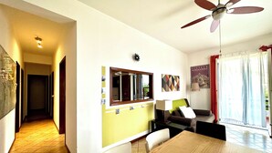 A dining area with a wooden table and chairs, a ceiling fan, and a kitchen area with a window and a poster on the wall. - Spacious and bright apartment with terrace and beautiful sea views (Aci Castello)